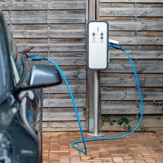 Point de recharge électrique pour voiture, câble branché sur un mur en bois.